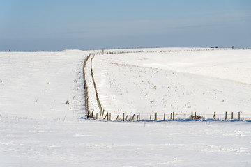 A snow-covered winter landscape, with a footpath running between two fences