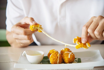 Man is going to eat sticky stretch fried cheese ball. Photo is focused at cheese ball