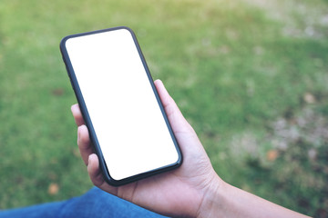 Mockup image of a woman holding and using black smart phone with blank white desktop screen in outdoor with green nature background