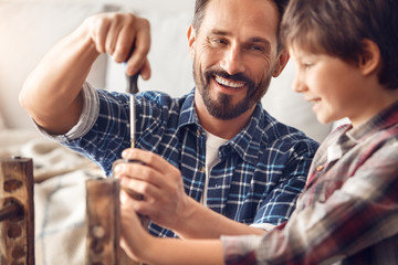 Wall Mural - Father and little son at home standing dad screwing screw laughing happy looking at boy holding chair leg close-up