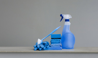 Cleaning blue spray bottle with plastic dispenser, sponge, .scrubbing brush for dish, cloth for dust and rubber gloves  on grey background. Cleaning equipment. Copy space.