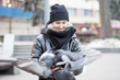 Birds doves eat sunflower seeds from the hands of a beautiful young girl in a black jacket and hat against a blurred background of the street.
