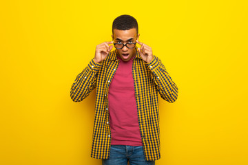 Wall Mural - Young afro american man on yellow background with glasses and surprised