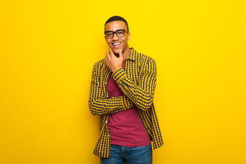 Wall Mural - Young afro american man on yellow background with glasses and smiling