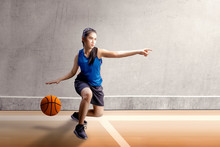 Beautiful Asian Woman In Sport Jersey Dribbling The Basketball With Left Arm Pointing In The Basketball Court
