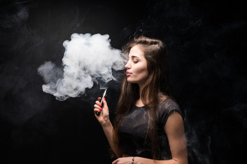 Attractive young woman vaping and blowing smoke isolated on black background