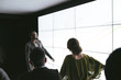 © JonoErasmus - Black african businesswoman giving a presentation at a business conference. Large video screen with charts and graphs next to her