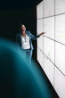 © JonoErasmus - Black african businesswoman giving a presentation at a business conference. Looking at a large video screen with charts and graphs next to her in a dark room