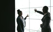© JonoErasmus - Silhouette of a black african business people giving a presentation conference. Pointing at a large video screen with charts and graphs next to her in a dark room