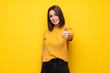 © luismolinero - Young woman over yellow wall with thumbs up because something good has happened