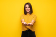 © luismolinero - Young woman over yellow wall holding copyspace imaginary on the palm to insert an ad