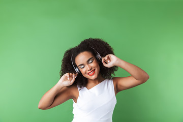 Poster - African woman posing isolated over green wall background listening music with headphones.