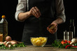 © Anton - The chef sprinkles french fries with herbs on a background with vegetables. Making tasty but harmful food. Background for design and menu.