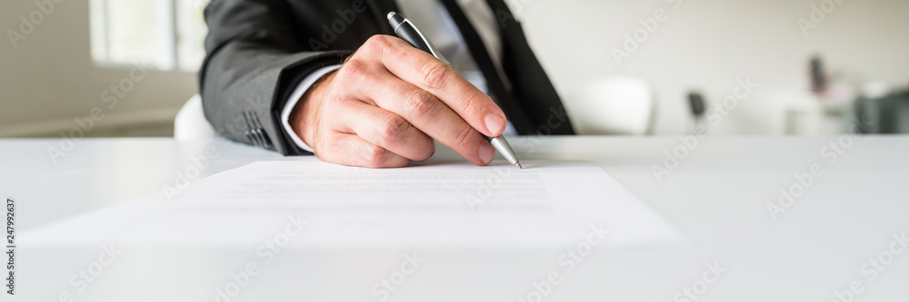 Wide view image of businessman sitting at his office desk signing a document - obrazy, fototapety, plakaty 