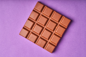 Bar of milk chocolate on a colored paper background