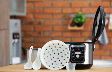 Sticker - Modern electric multi cooker, parts and accessories on table in kitchen. Space for text