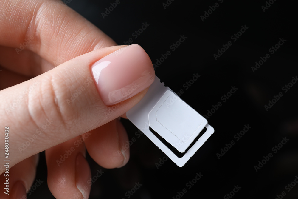 Female hand holding sim card on dark background