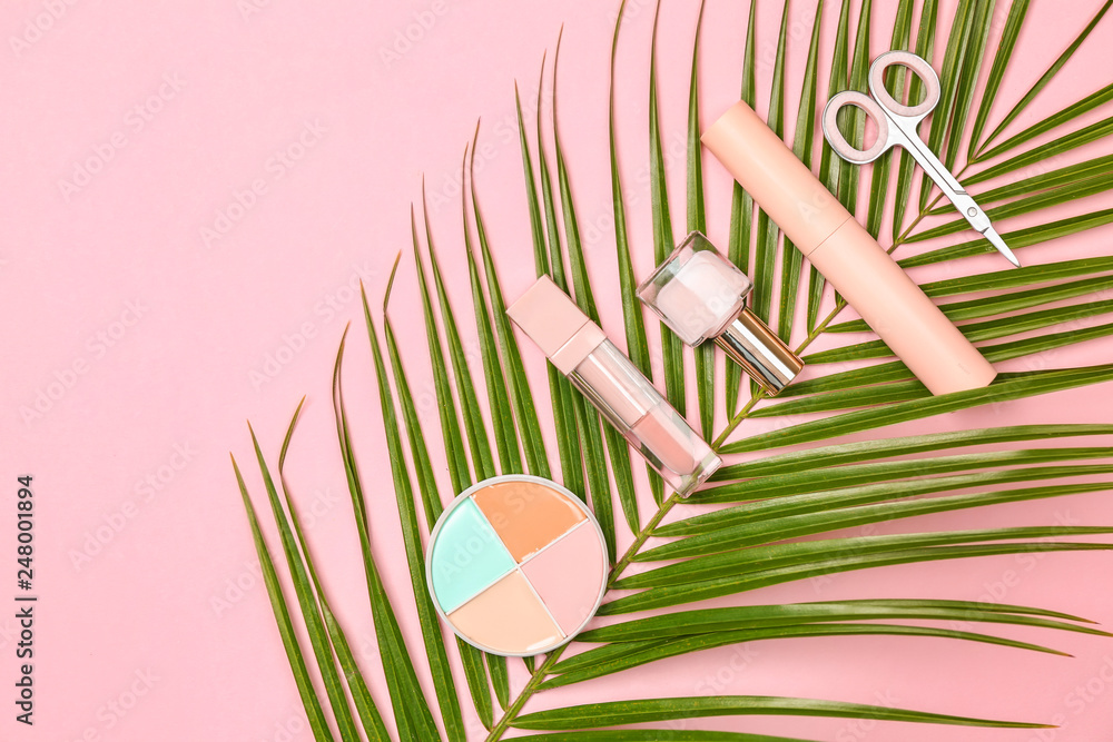 Set of makeup cosmetics with palm leaf on color background