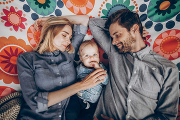 Cute family resting on boho hammock with smiling baby boy, young hipster family on camping trip lying on hammock outdoors