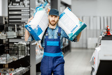 Portrait Of A Handsome Workman In Blue Overalls Holding Bags With Construction Mixture In The Building Supermarket