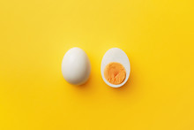 Single Whole White Egg And Halved Boiled Egg With Yolk On A Yellow Background. Top View