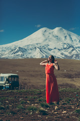 brunette slim girl in long red dress on the background of high snow-capped mountains 