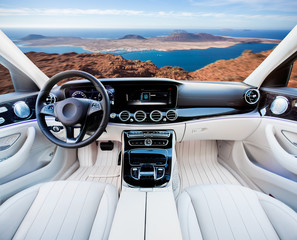 Dark car Interior - steering wheel, shift lever and dashboard. Car modern inside. Front view on sunset and sea background. The sun shines in the glass.glare