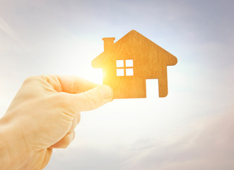 Man's hand holds wooden flat house against the sun