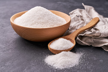 Bowl and  wooden spoon full of  white sugar on black background