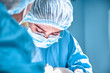 © Georgii - Close up portrait of young female surgeon doctor wearing protective mask and hat during the operation. Healthcare, medical education, surgery concept