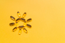 Close Up Capsules Of Fish Fat Oil In The Sun Shape, Omega 3, Vitamin E On The Yellow Background. Healthy Food Diet. Nutritional Supplement