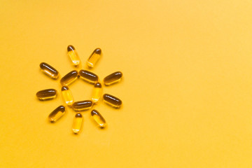 Close up capsules of fish fat oil in the sun shape, omega 3, vitamin e on the yellow background. Healthy food diet. Nutritional supplement