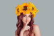 © hbrh - Shh. Young woman with floral headband smiling with a finger to her lips hush sign gesture. Concept for silence. Fashion girl, crown from sunflowers on head isolated on gray background with copyspace.