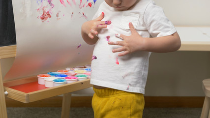 Cute little boy (toddler, two years old) is painting on tee. Washable finger paints for Babies Kids, art, creative. Dirty cloth (t-shirt), washing laundry concept.