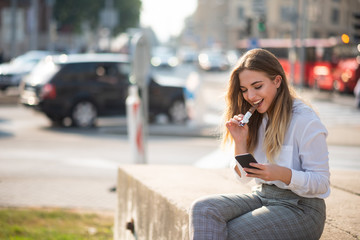 Girl biting sweet chocolate bar and checking mobile phone