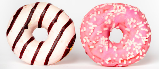 two donuts isolated on a white background, one pink with white sprinkles and the other one with strips of white and dark chocolate