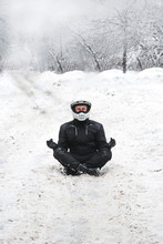 Rider Man Is Sitting On Snowy Road Alone. Meditating In The Lotus Position That Used To End The Winter. Travel Tour, Active Life Style Concept. Winter Clothes, Equipment, Vertical Photo