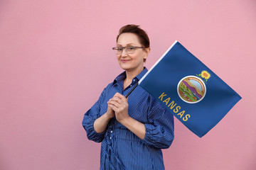 Wall Mural - Kansas flag. Woman holding Kansas state flag. Nice portrait of middle aged lady 40 50 years old holding a large state flag over pink wall background on the street outdoor.