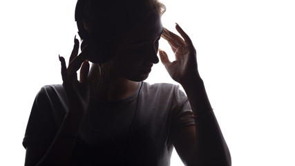 Wall Mural - silhouette of a romantic girl listening to music in headphones, young woman relaxing on a white isolated background, concept of hobby and leisure