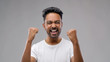 success, emotion and expression concept - happy young indian man celebrating victory over grey background