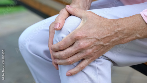 Cuadros en Lienzo Old lady touching knee, sitting on bench, pain in joints, problems with knees