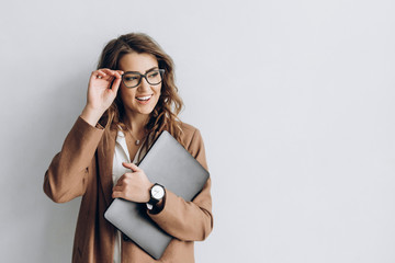 Beautiful business woman in a glasses with smile and a laptop in her hands in the office near a white wall with blank space for text