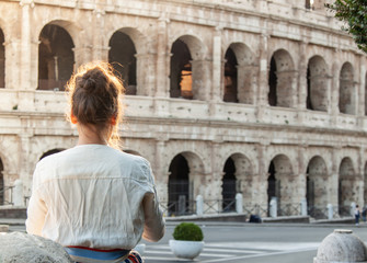 Beautiful young woman in fashion dress alone in front of colosseum in Rome at sunset.