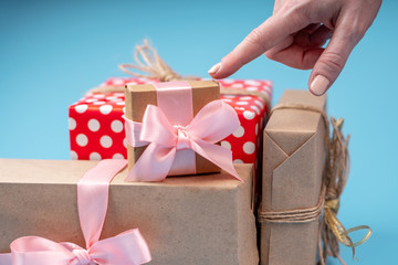 Wall Mural - Hands holding gift boxes Packed in Kraft paper with pink ribbon on blue background. Holiday card for Valentine's day