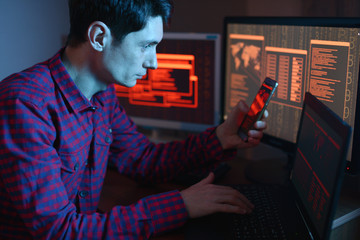 Wall Mural - Hacker holding the phone in his hands trying to hack the mobile device cloud and steal data in the dark under neon light