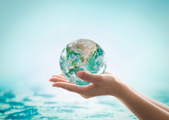 World ocean day, saving water campaign, sustainable ecological ecosystems concept with green earth on woman's hands on blue sea background : Element of this image furnished by NASA .