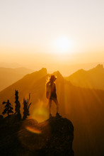 Rear View Of Person Standing On Mountain Edge During Sunset