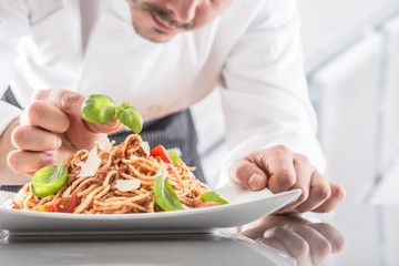 Chef in restaurant kitchen prepares and decorates meal with hands.Cook preparing spaghetti bolognese