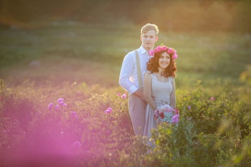 Wall Mural - Happy young couple man and woman, adult romantic family. Meet the sunset in a wheat field. Happy smiling. The girl in her hands holds a gift, a bouquet of flowers, from roses.