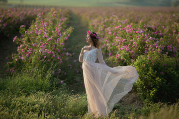 Young beautiful girl in a long dress and a wreath of flowers in the garden of lilac bush